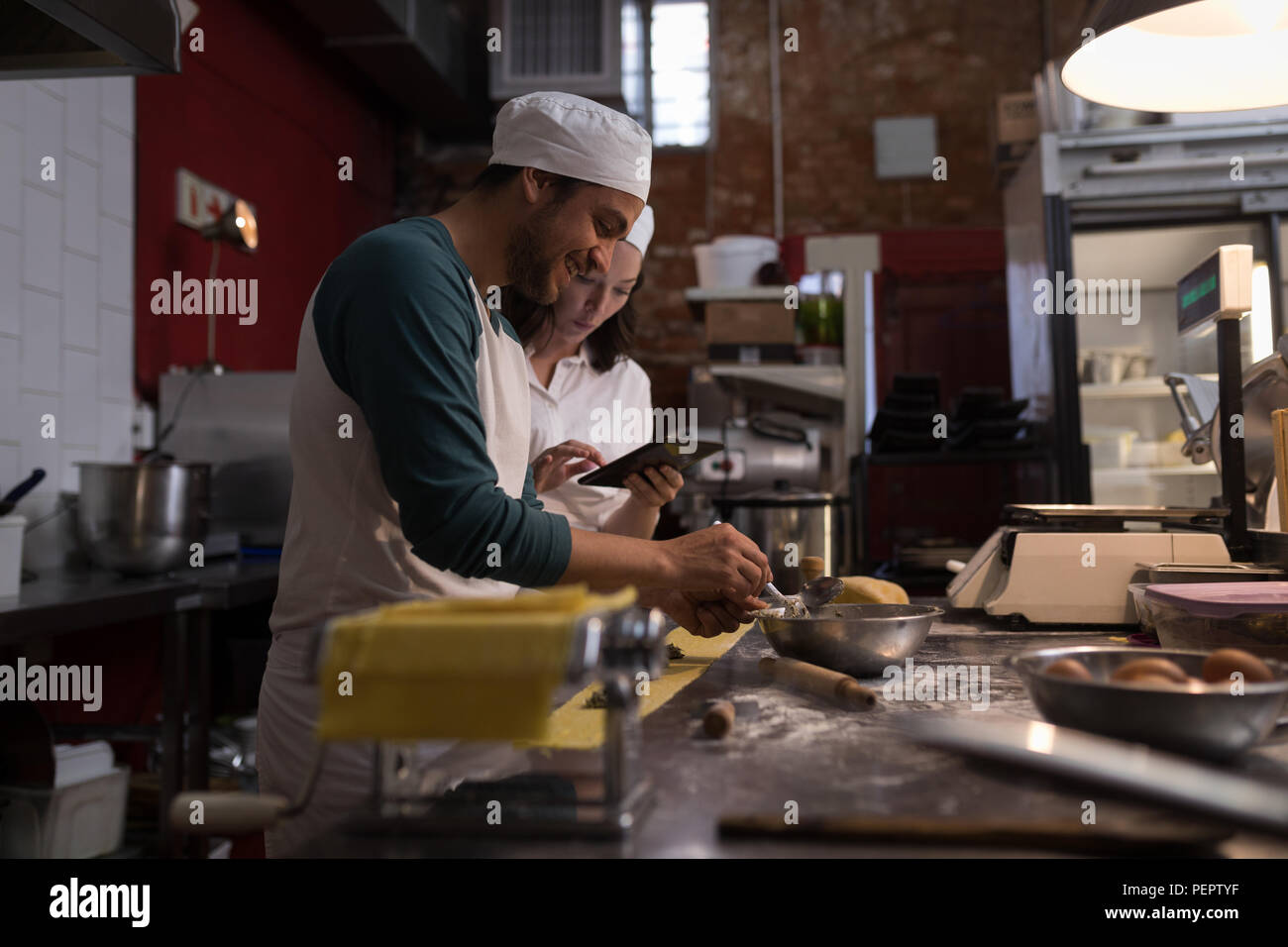Baker Vorbereitung Pasta während die Co-worker mit digitalen Tablet seine neben Stockfoto