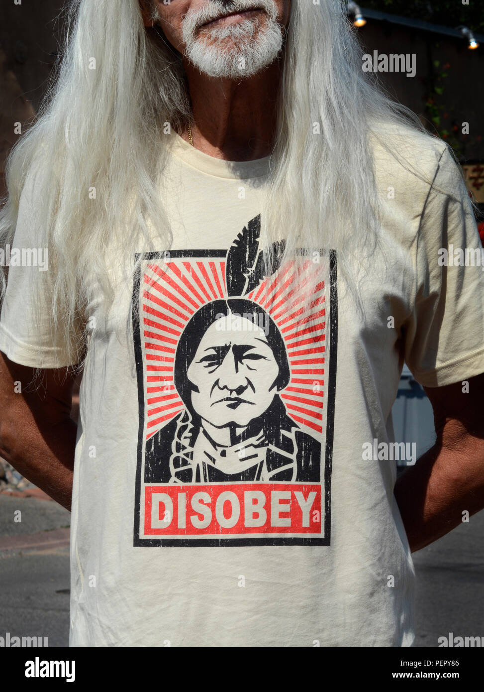 Ein Mann mit einem Bart und langes Haar trägt ein T-Shirt Bedruckt mit einem Bild von Sitting Bull und das Wort "ISOBEY'. Stockfoto
