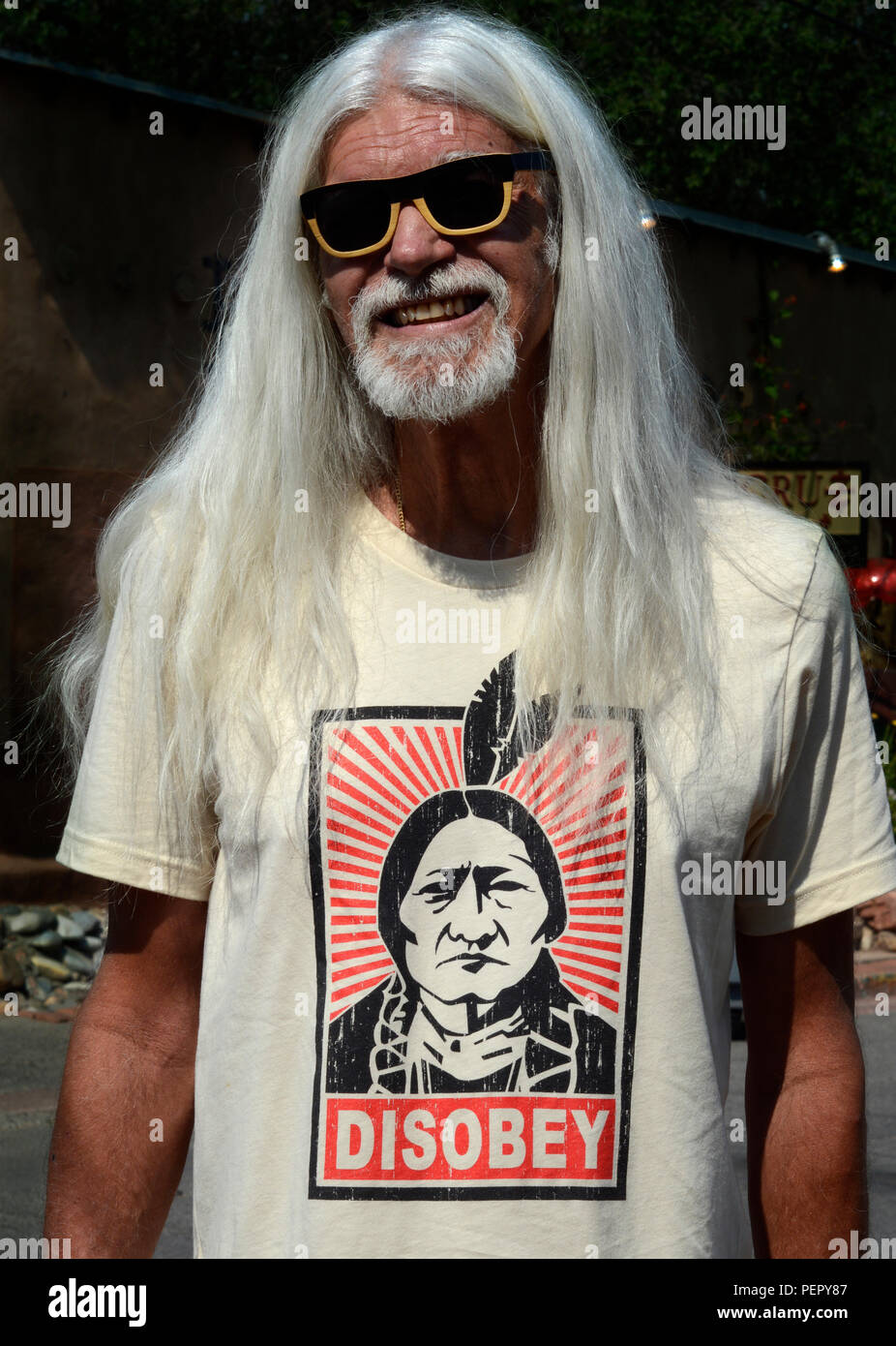 Ein Mann mit einem Bart und langes Haar trägt ein T-Shirt Bedruckt mit einem Bild von Sitting Bull und das Wort "ISOBEY'. Stockfoto