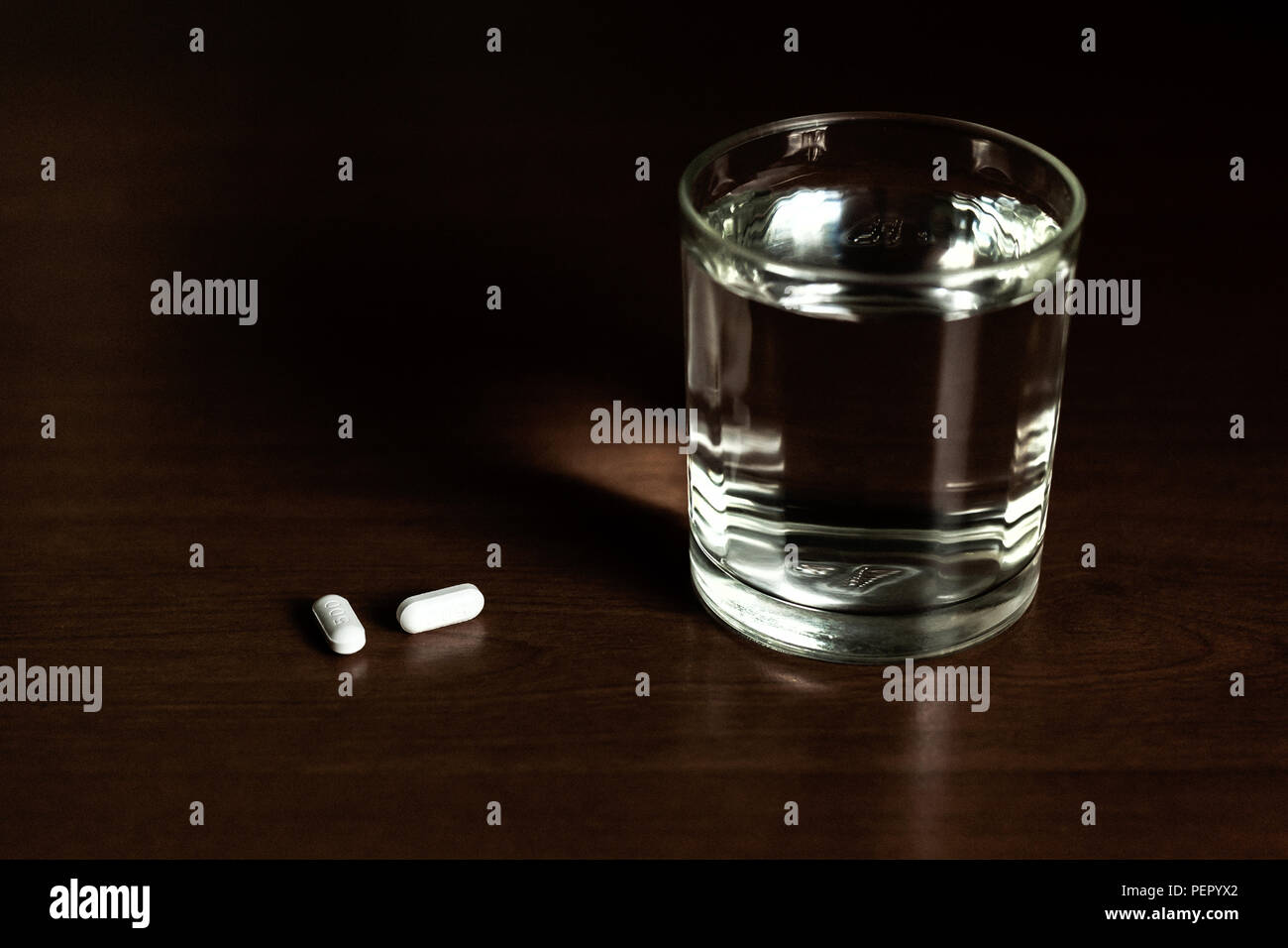 Konzeptionelle Glas Wasser und Pillen auf hölzernen Tisch in kreativen Desturated Kontrast. Stockfoto