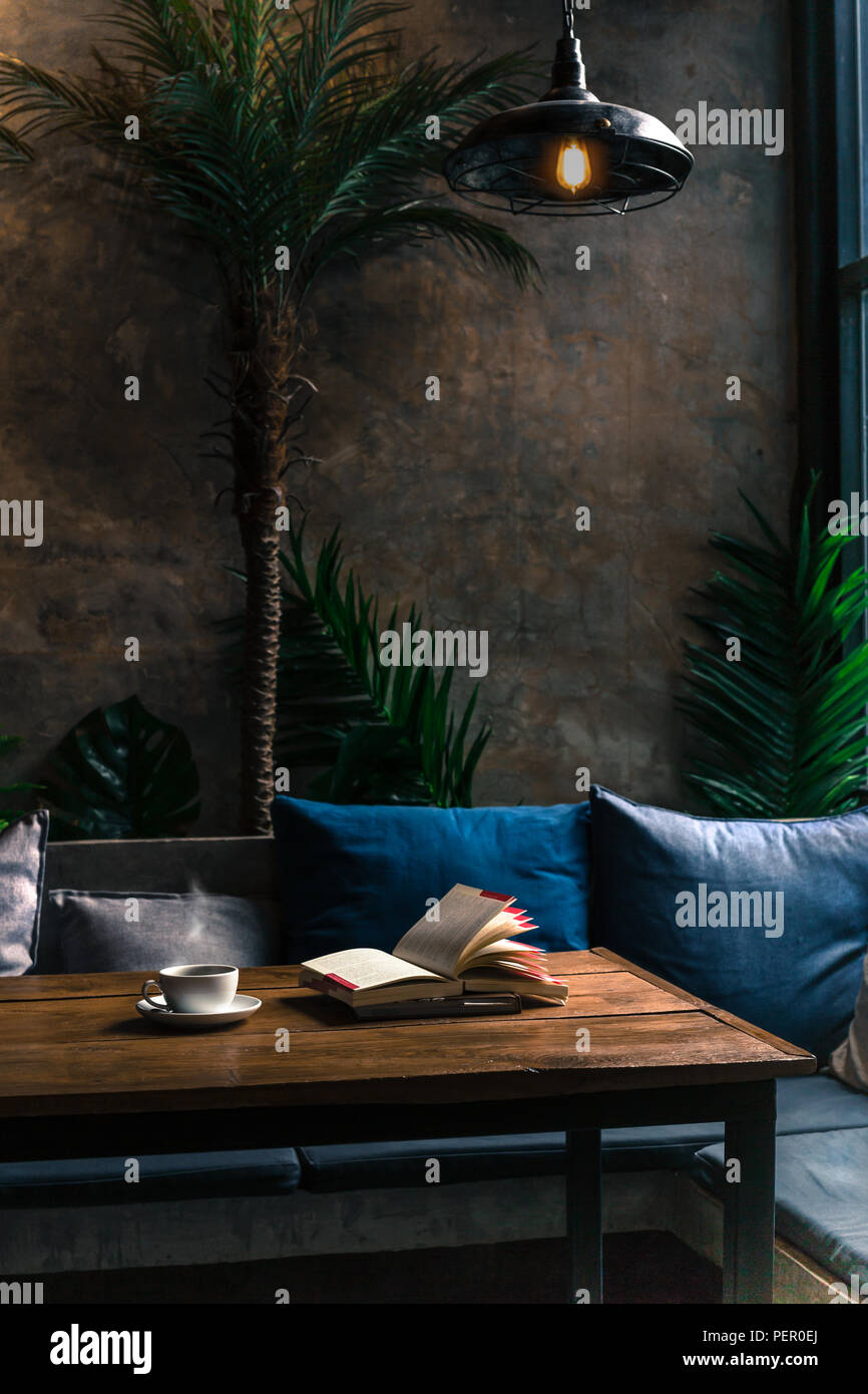 Konzeptionelle in dunklen Ton Kaffeetasse und Bücher auf hölzernen Tisch unter der Lampe. Stockfoto