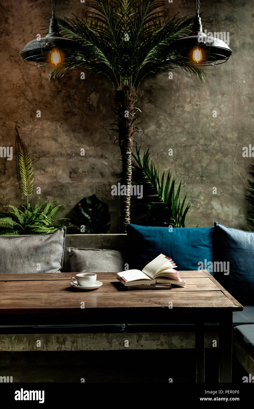 Konzeptionelle in dunklen Ton Kaffeetasse und Bücher auf hölzernen Tisch unter der Lampe. Stockfoto