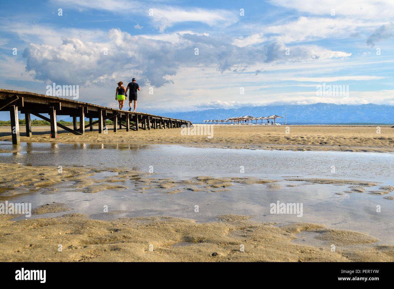 Ein Paar zu Fuß über eine Holzbrücke mit der berühmten Queens Strand in Nin in der Nähe von Zadar, Kroatien. Seltene sand Strand der Adria, beliebt für surfin Stockfoto