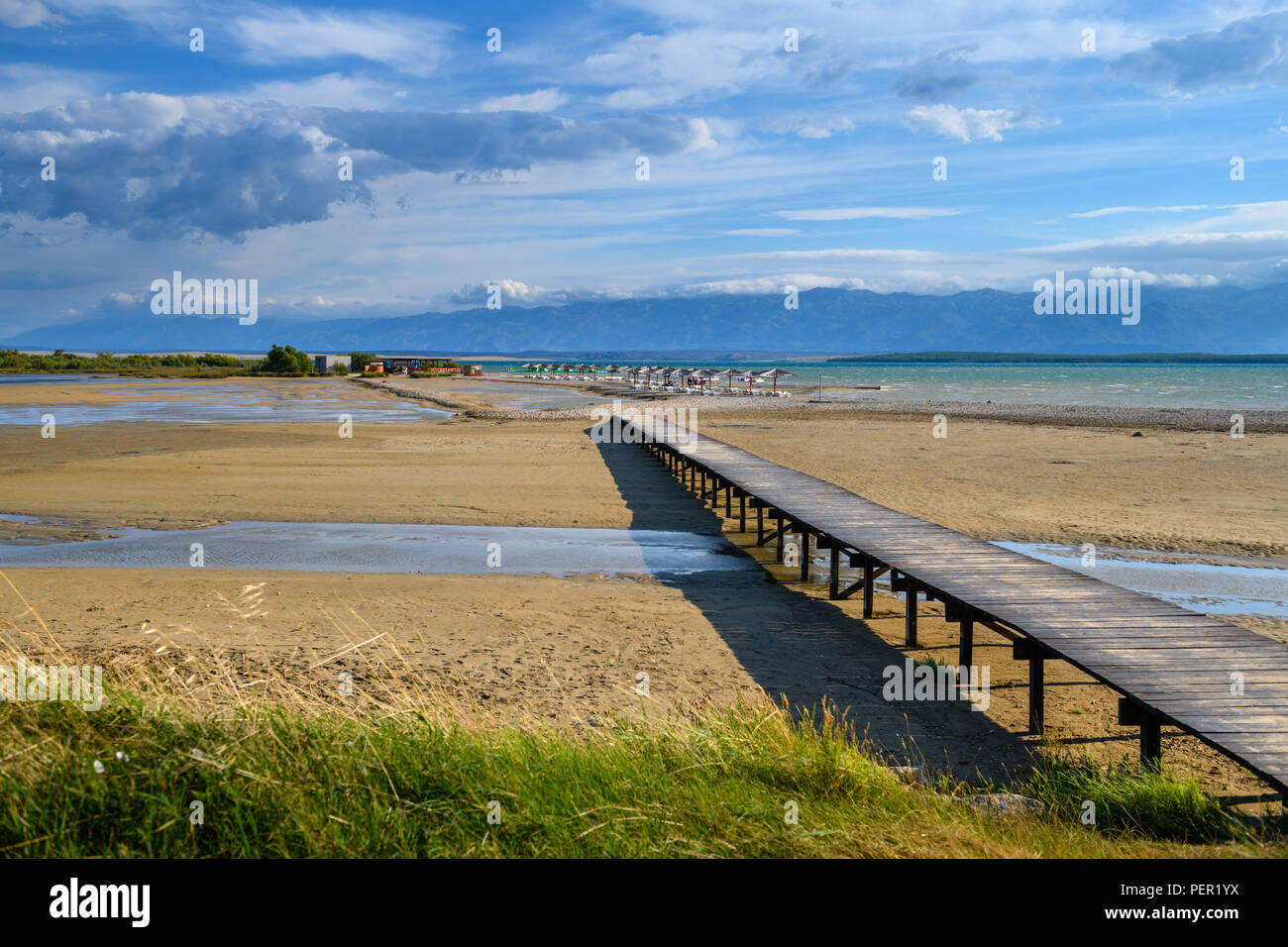 Ein Paar zu Fuß über eine Holzbrücke mit der berühmten Queens Strand in Nin in der Nähe von Zadar, Kroatien. Seltene sand Strand der Adria, beliebt für surfin Stockfoto