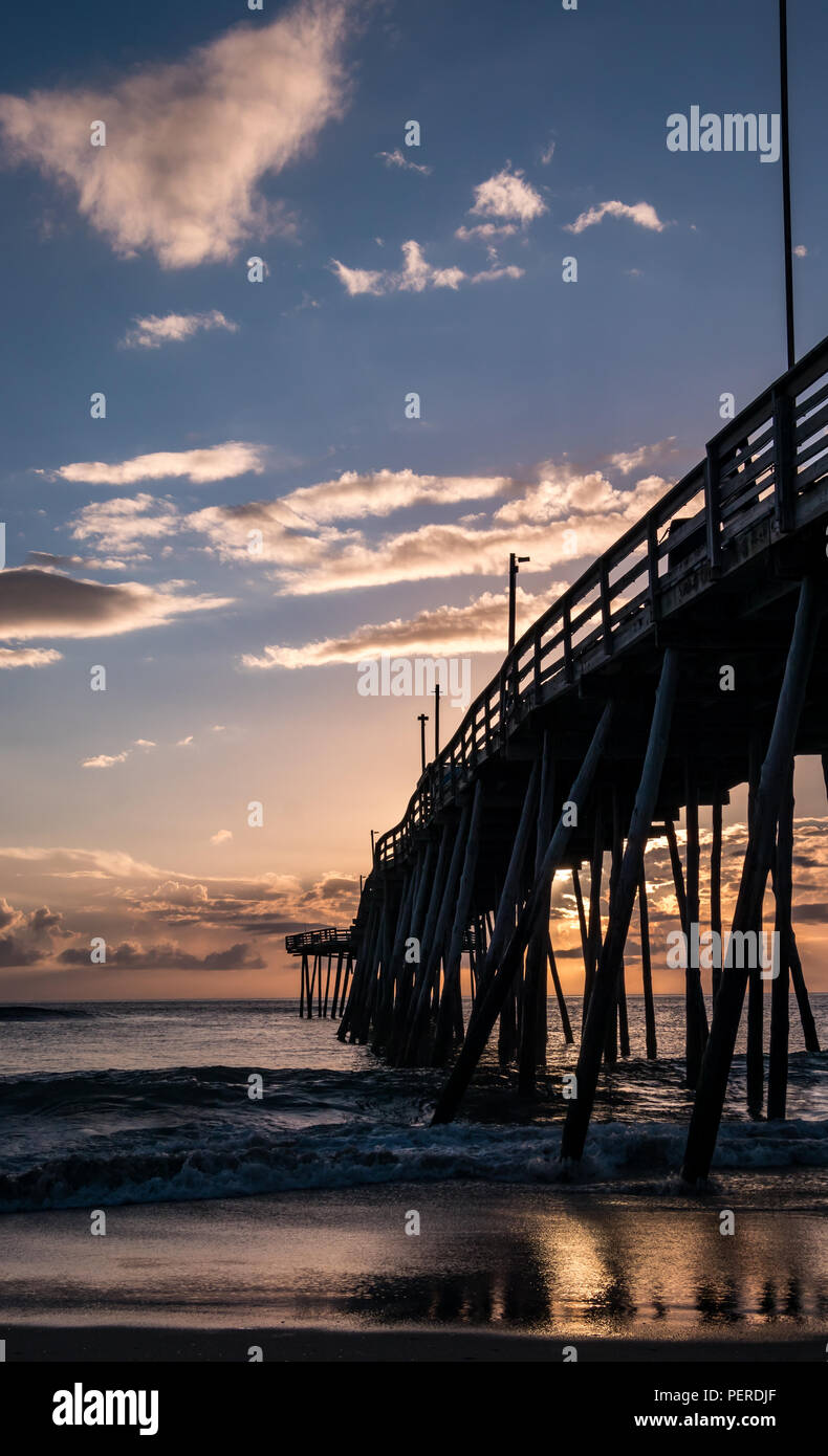 Ein dramatischer Sonnenaufgang Himmel voller rosa und violetten Tönen über einen ruhigen Meer. Die Farben des Himmels sind im Wasser unter einem hölzernen Fishing Pier wider. Stockfoto