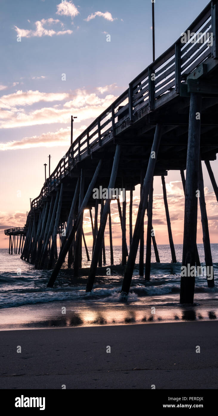 Wunderschöne rot und pink sunrise in das Wasser unter einem hölzernen Fishing Pier wider. Stockfoto