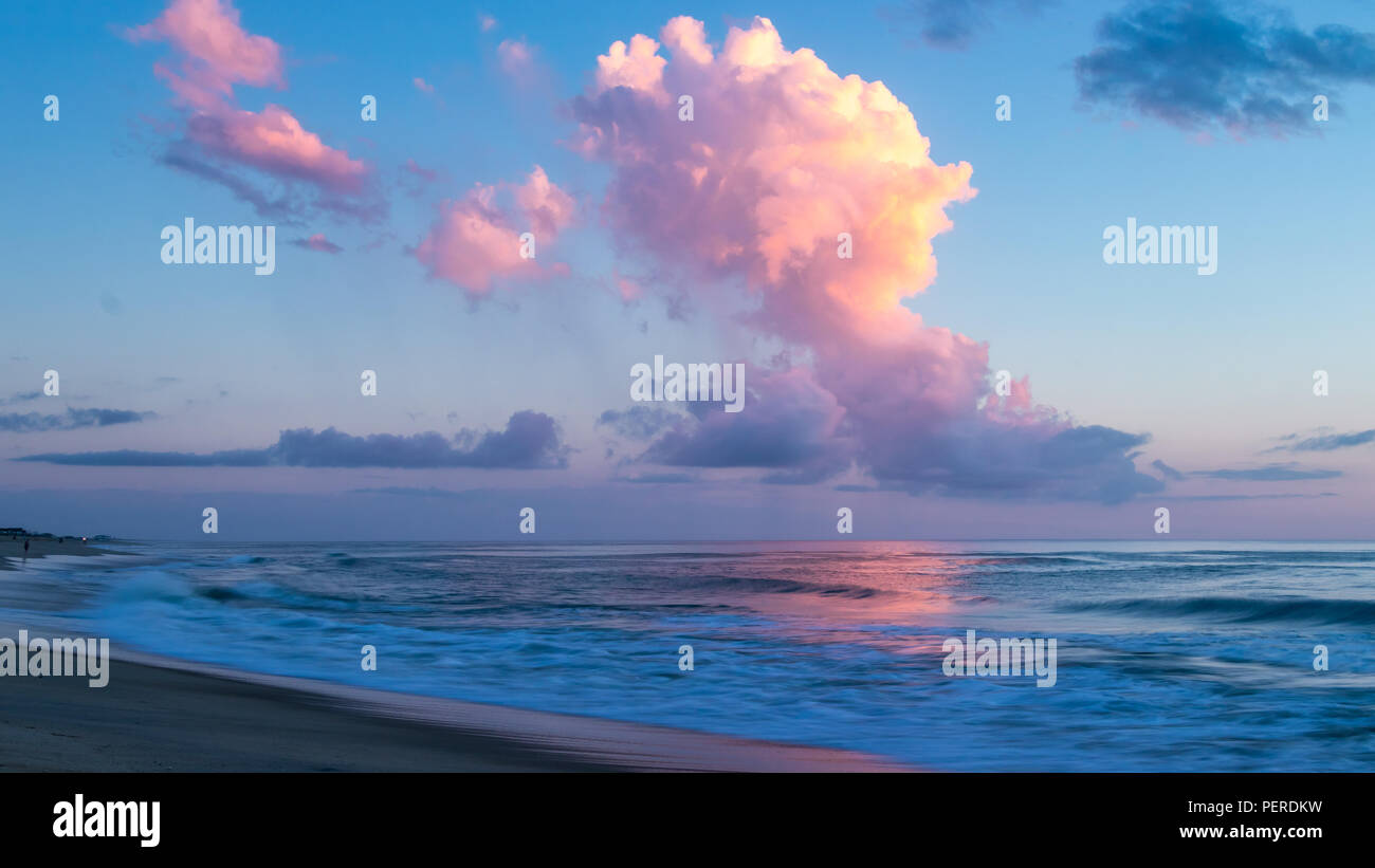 Die Pastellfarben der einen wunderschönen Sonnenaufgang über einer ruhigen Meer. Am Morgen Licht auf der Oberfläche des Meeres und auf dem nassen Sand eines leeren Strand wider. Stockfoto
