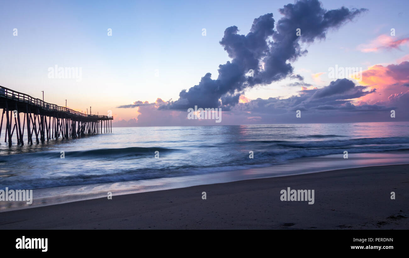 Hell Lila, Blau und Magenta dramatische Morgenhimmel. Ruhiges Meer Wasser spiegelt die sunrise Farben. Lange Belichtung für weiches, Weichzeichner auf dem Wasser. Stockfoto