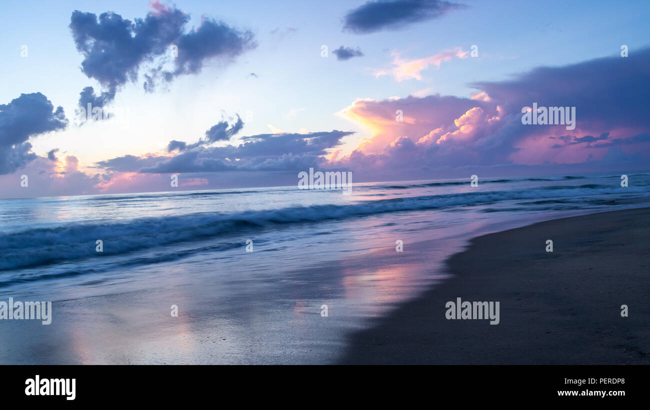 Die Pastellfarben der einen wunderschönen Sonnenaufgang über einer ruhigen Meer. Am Morgen Licht auf der Oberfläche des Meeres und auf dem nassen Sand eines leeren Strand wider. Stockfoto