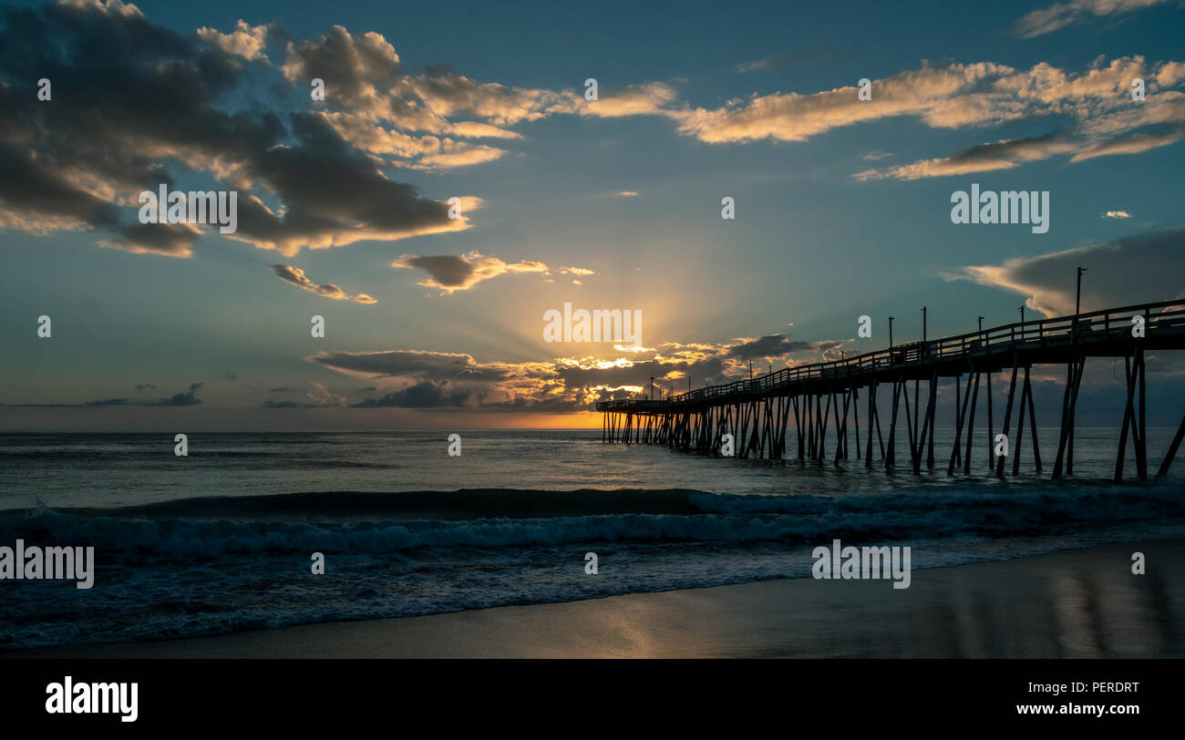 Sonnenaufgang hinter dem Ende einer Holz- Fishing Pier. Lichtstrahlen Strahl hinter Wolken. Stockfoto