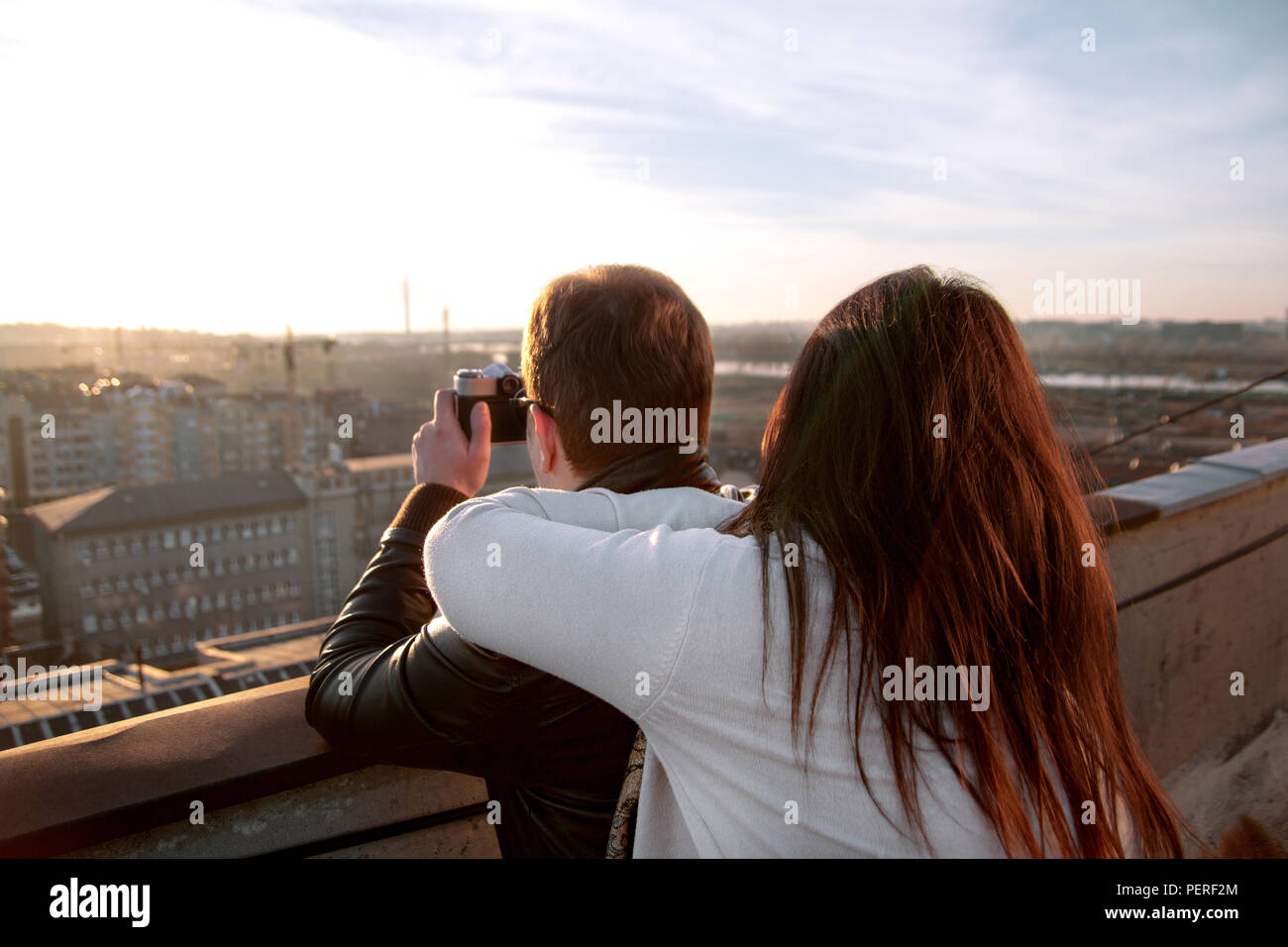 Paar Fotos von den Sonnenuntergang auf der Dachterrasse der Stadt. Paar genießt die Sonne auf dem Dach und ein junger Mann fotografieren Panorama der Stadt. Stockfoto