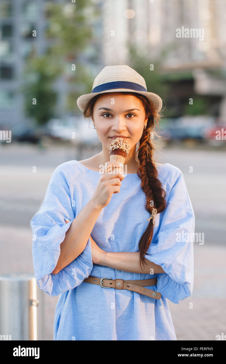 Porträt der schönen Happy white Kaukasischen brunette Mädchen Frau mit Grübchen auf den Wangen und gebräunte Haut in blauem Kleid und Hut essen Eis Kegel, su Stockfoto