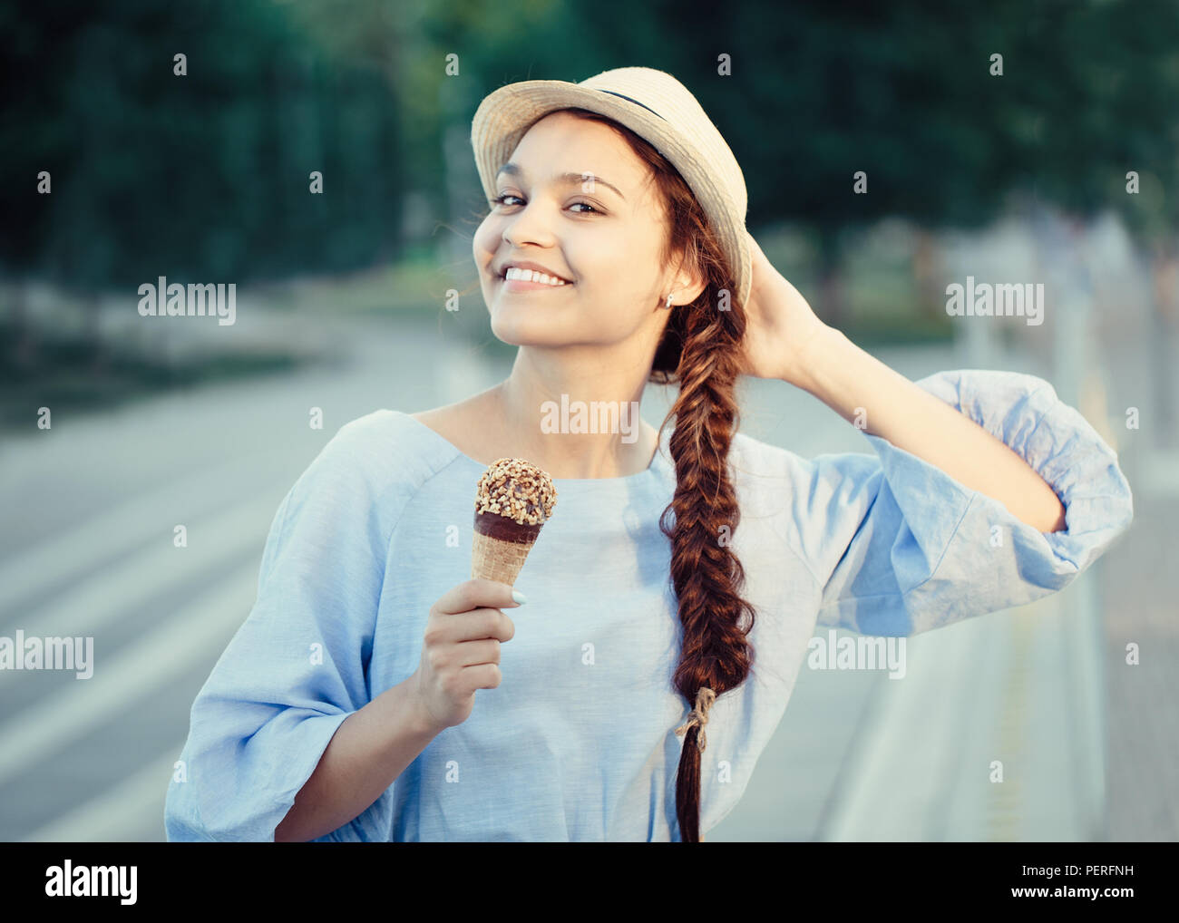 Closeup Portrait von schönen Happy white Kaukasischen brunette Mädchen Frau mit Grübchen auf den Wangen und gebräunte Haut in blauem Kleid und Hut, Eis essen Stockfoto