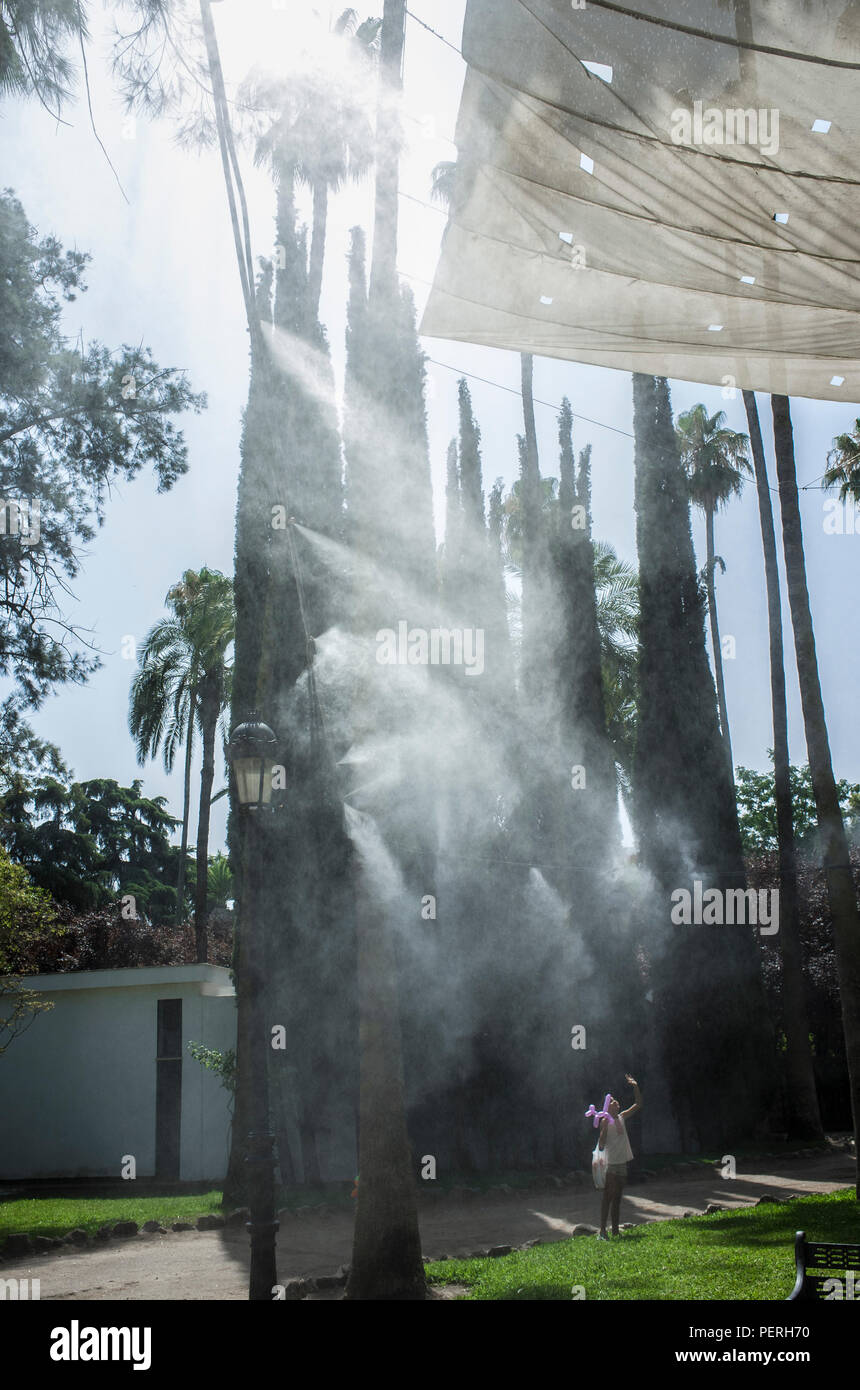 Kind Mädchen genießen unter Sprinklern spritzt verdampft Wasser bei öffentlichen Park. Geräte für die Kühlung der heißen Sommer Temperatur in Spanien im Freien Stockfoto