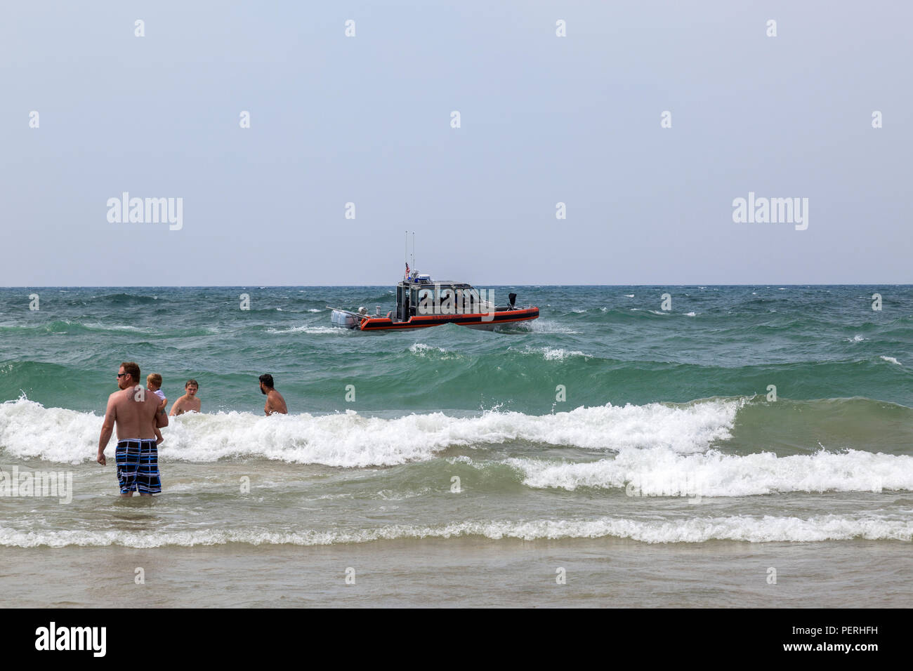 Mann und Jungen stehen in See mit Wellen, wie die Küstenwache Boot vorbei geht. Dies ist in Muskegon, Michigan, USA. Stockfoto