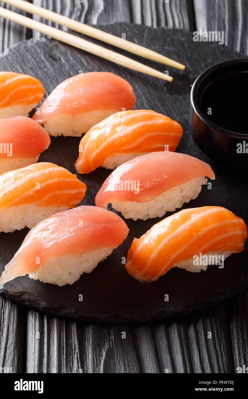 Sushi mit Lachs und Thunfisch, Sojasauce close-up auf einem schwarzen Schiefer auf einem Tisch. Vertikale Stockfoto
