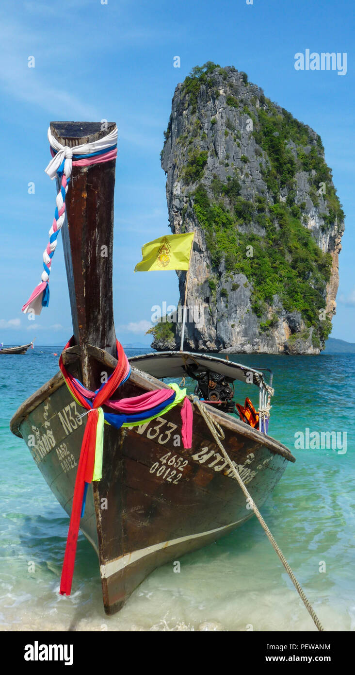 Hochformat eines traditionellen Long tail Boot mit Thai Fahnen an einem der Strände von Krabi in Thailand warten, mit Kalkfelsen an der Rückseite Stockfoto