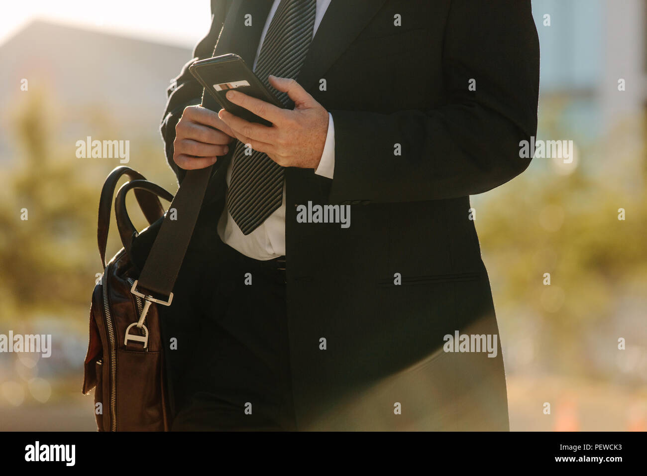 Den mittleren Abschnitt eines Mannes in formelle Kleidung mit seinem Handy, während das Pendeln zum Büro. Büro Mann zu Fuß auf der Straße und mit seinem mobilen Stockfoto