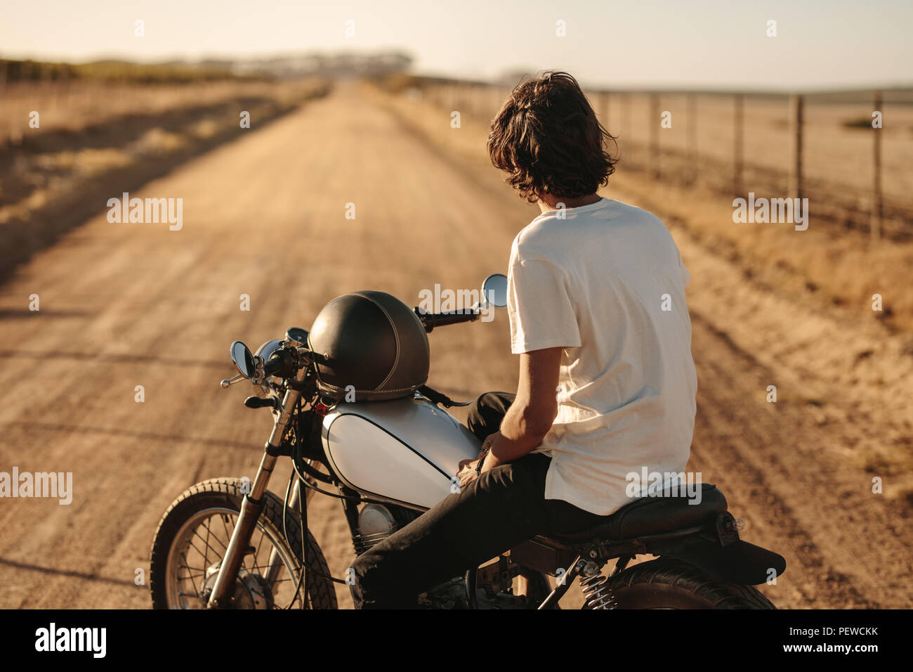 Ansicht der Rückseite des jungen Mann sitzt auf seinem Fahrrad und auf leere Landstraße. Junge Motorradfahrer auf seinem Fahrrad und Blick auf die ländliche Straße. Stockfoto