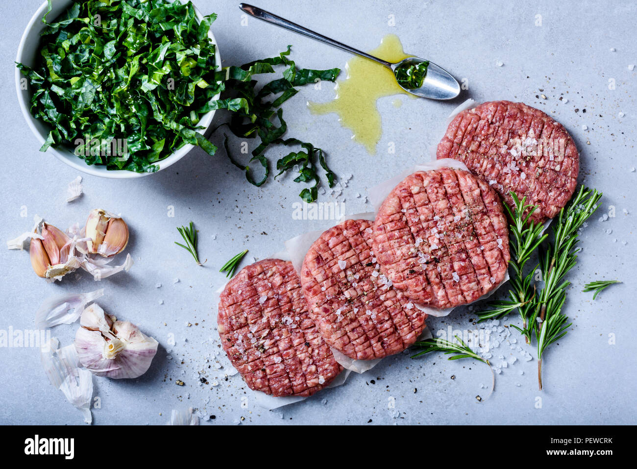 Rohes Rindfleisch hamburger Pastetchen mit Salat, Kräuter und Gewürze, gesundes Kochen, grau konkreten Hintergrund Stockfoto