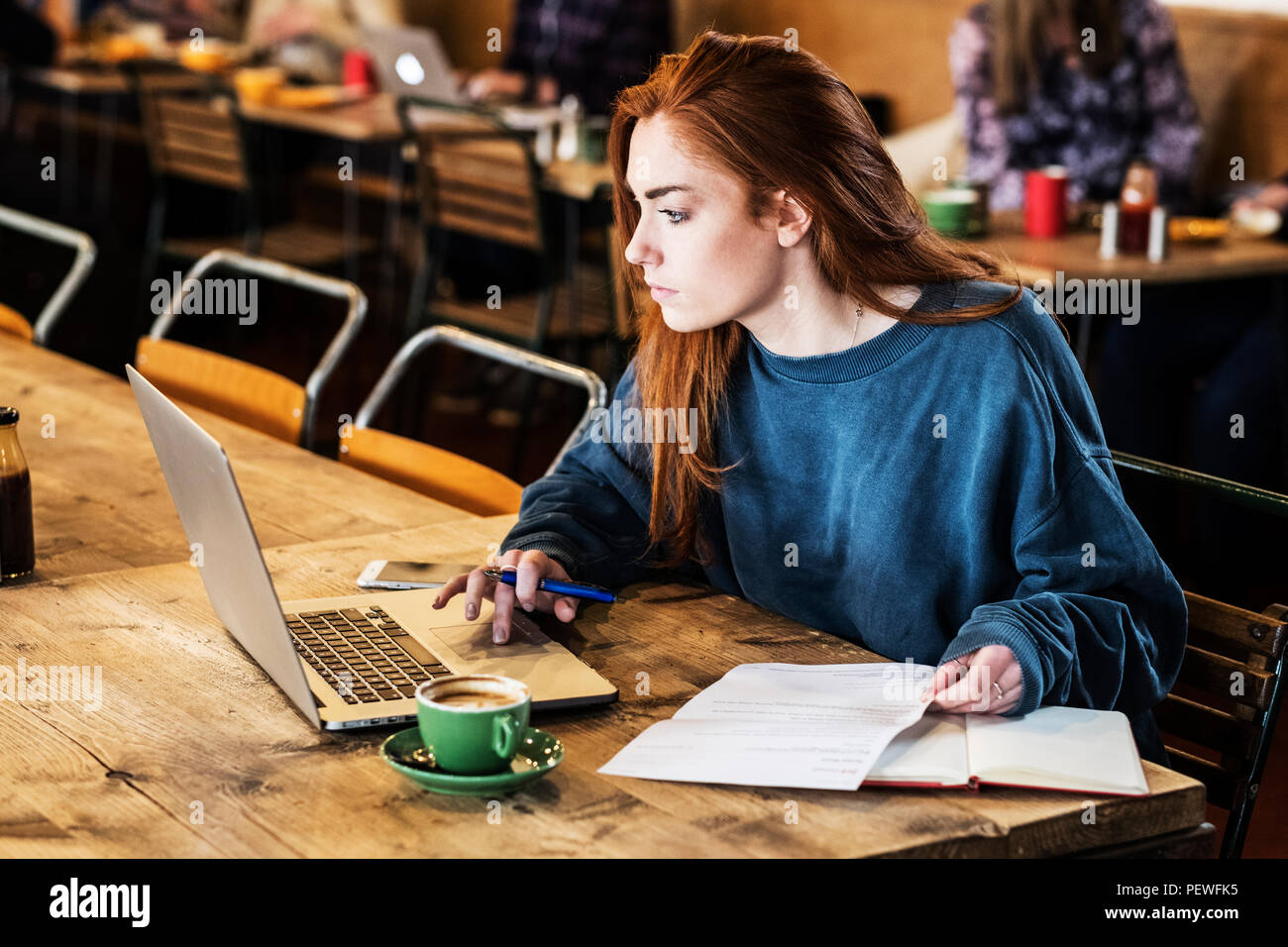 Junge Frau mit langen roten Haaren sitzen am Tisch, Arbeiten am Laptop. Stockfoto