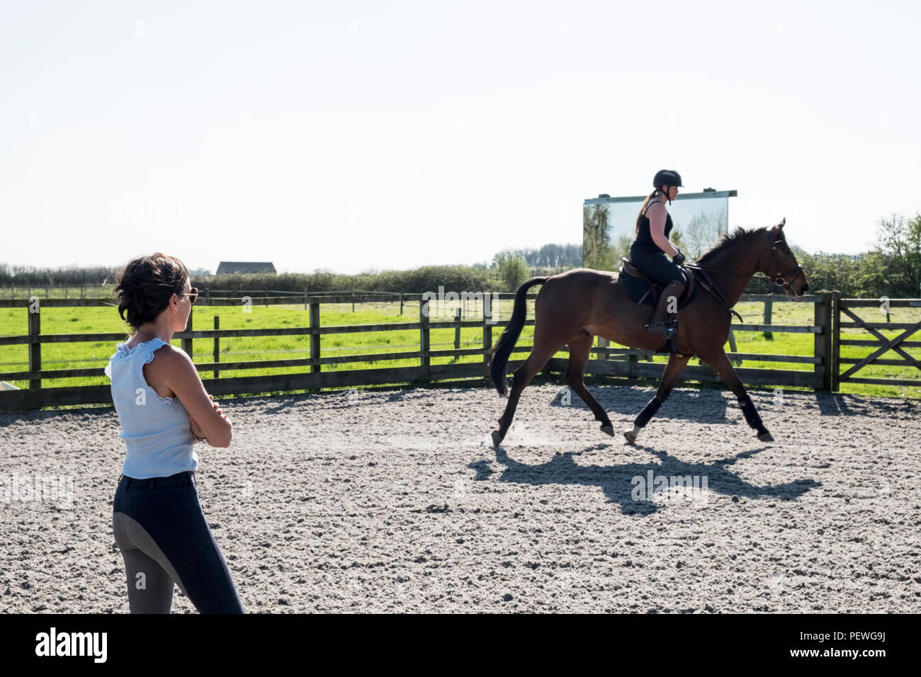Frau, ein Pferd Trainer beobachten, eine junge Frau, die auf einem braunen Bay Horse in einer Schule. Stockfoto