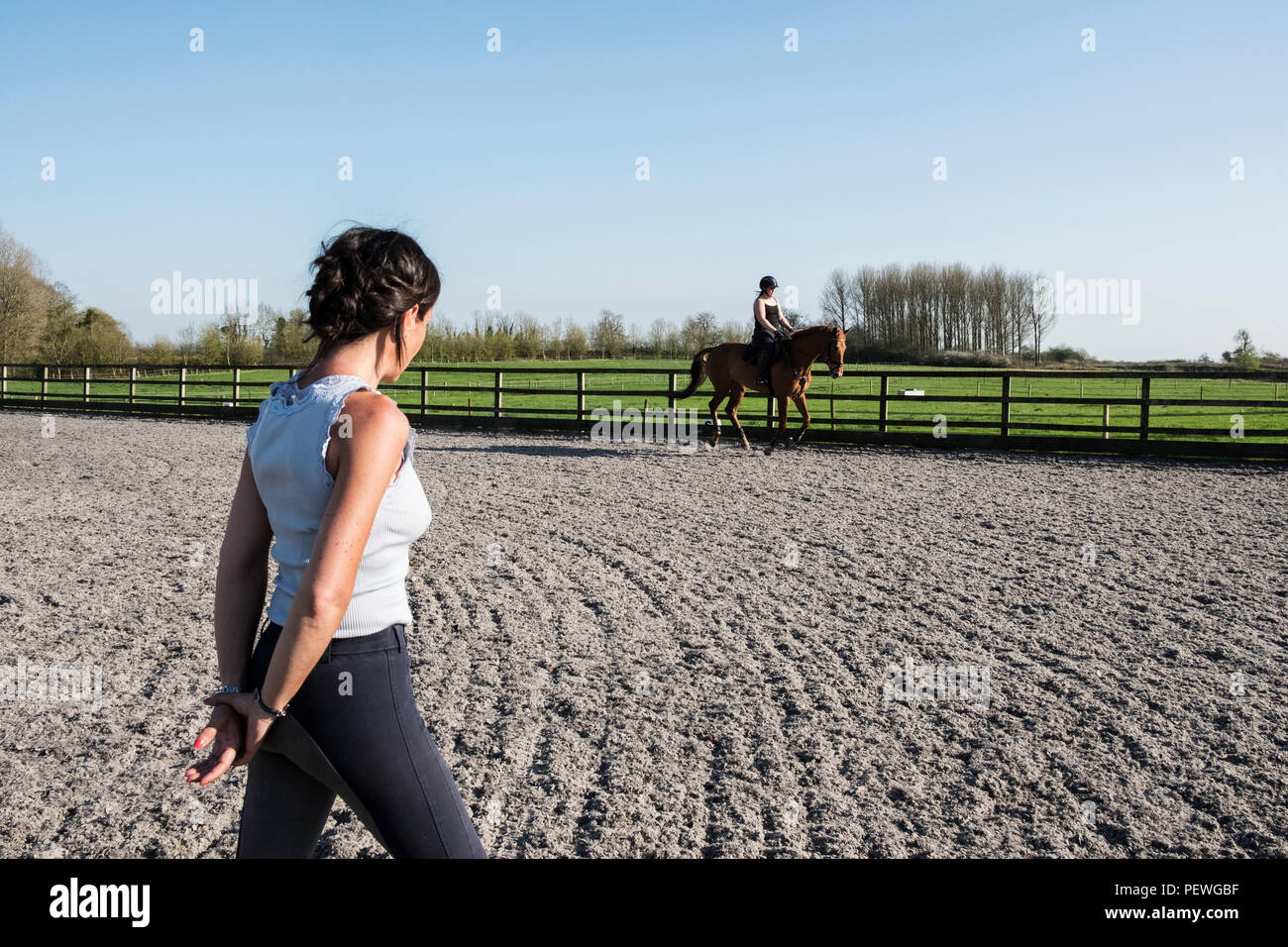 Frau trainer Beobachten ein Jugendmädchen Reiten auf einem Pferd baybrown im Paddock. Stockfoto