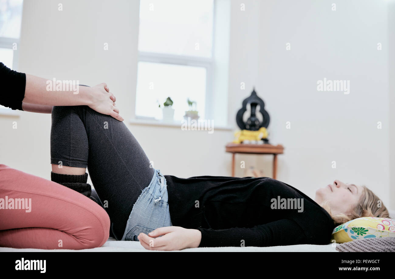 Frau liegend auf dem Rücken und einem thailändischen massagew practioner sanft ihre Knie und Beine strecken. Stockfoto