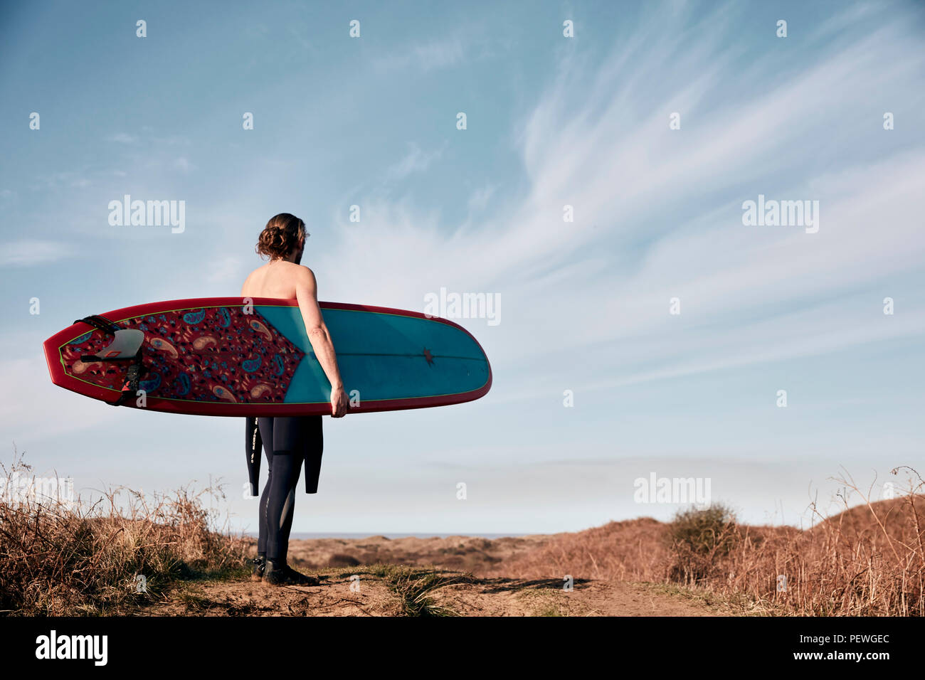 Mann zu Fuß auf den Weg in die Dünen in Richtung Meer mit einem Surfbrett. Stockfoto