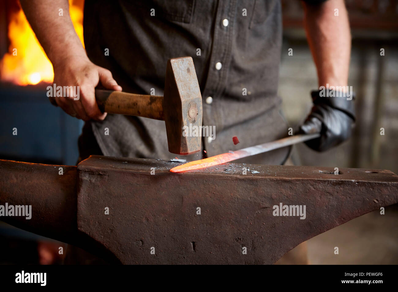 Ein Handwerker Metallarbeiter in Gehörschutz mit einem Hammer ein red hot Stück Metall auf einen Amboss zu gestalten. Stockfoto