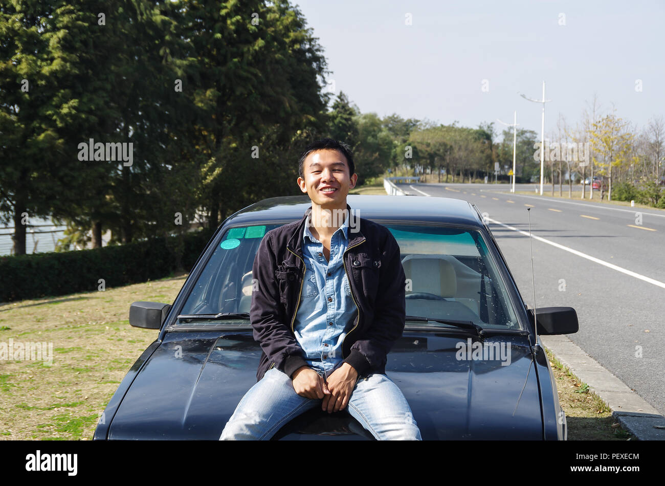 Ein chinesischer Junge Mann sitzt auf dem Auto Lächeln für die Kamera Stockfoto