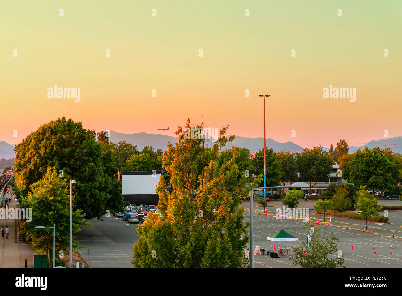 Parkplatz mit Sommerkino, grüne Bäume, Berge, Fliegen, Flugzeug, Autos auf Sommerabend in der modernen Stadt Stockfoto