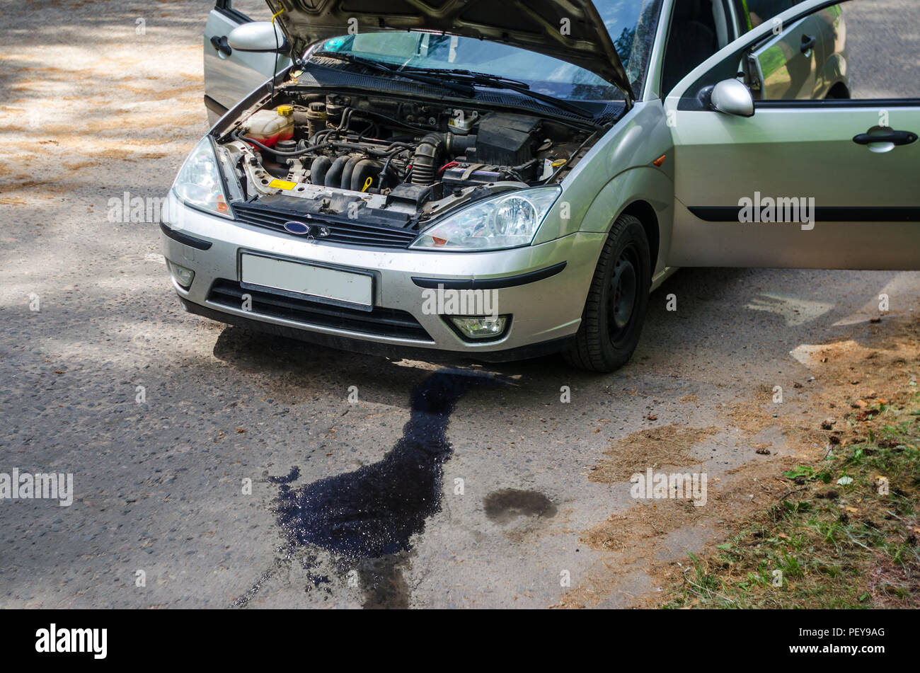 Gebrochene Auto auf den Straßenrand mit offener Motorhaube, Kofferraum und Türen. Auslaufen von Öl aus dem Motor auf dem Asphalt Stockfoto