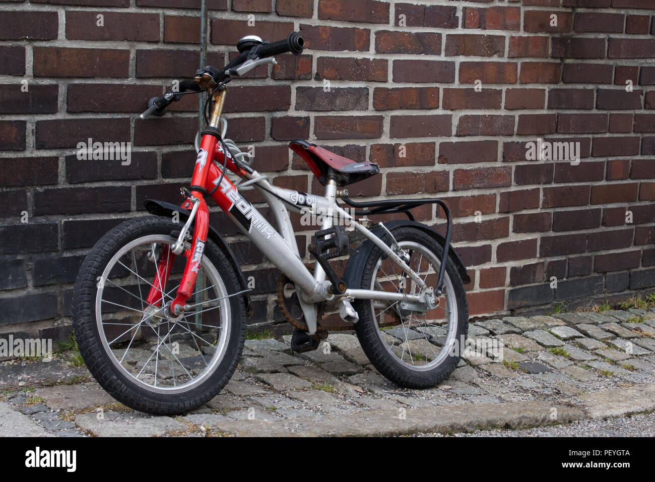 Kinder verwendet altes Fahrrad auf Kopfsteinpflaster Straße vor der Mauer Schule Gebäude geparkt Stockfoto