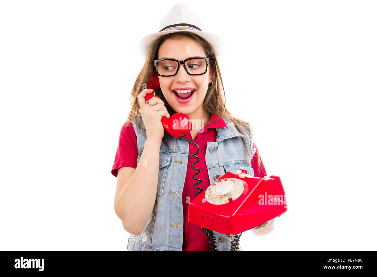 Trendige junge Frau mit Hut und Brille suchen beim Sprechen auf retro Telefon auf weißem Hintergrund überrascht Stockfoto