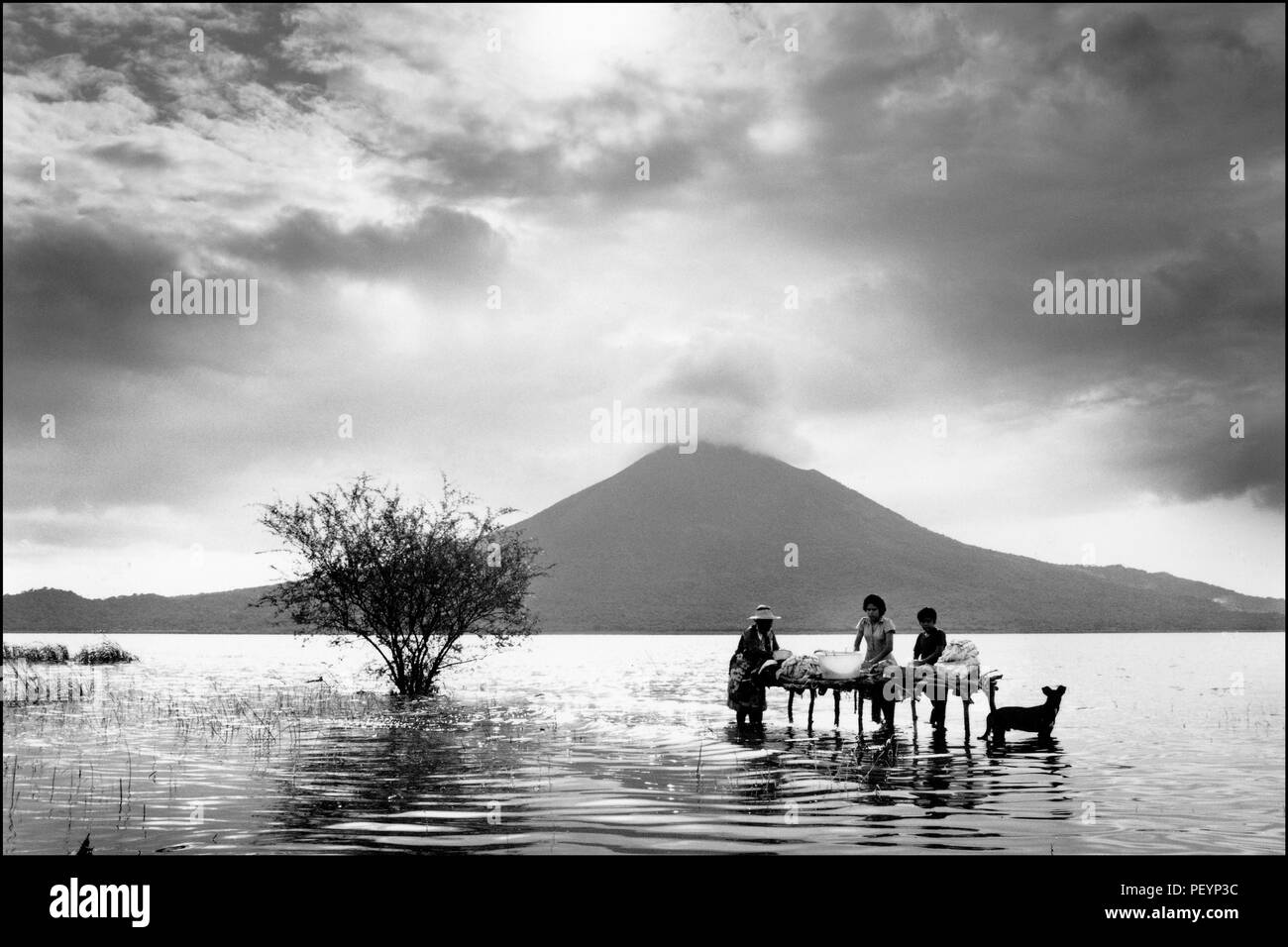 Eine Familie wäscht ihre Kleidung im Wasser des Managua Sees mit dem rauchenden Vulkan Momitombo dahinter. Stockfoto