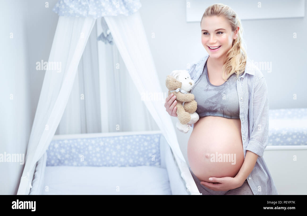 Schwangere Frau zu Hause niedlich, die zukünftige Mutter mit Zärtlichkeit berührt ihr Bauch, genießt die Vorbereitung ein Kinderzimmer für Ihr Kind, glückliche Mutterschaft co Stockfoto