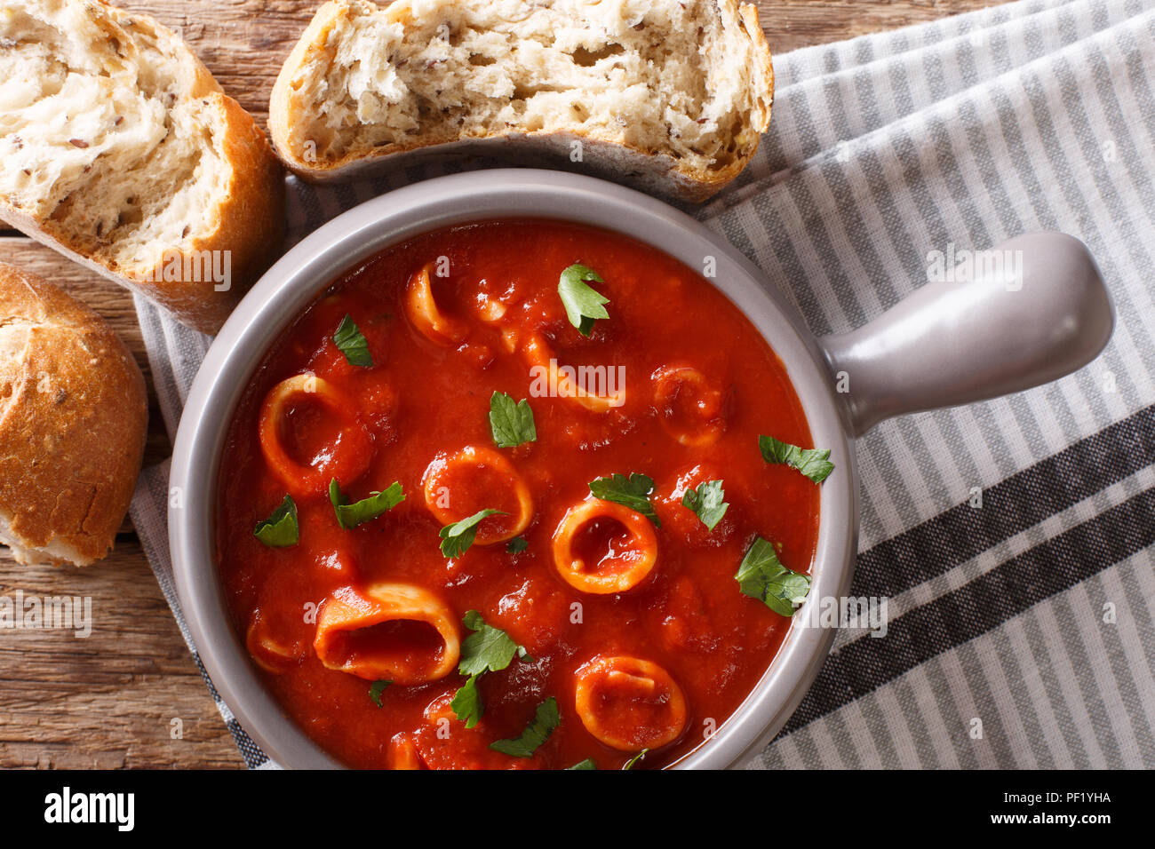 Traditionelle mediterrane Meeresfrüchte Tintenfischringe in Tomaten mit Gewürzen und Petersilie close-up in einem Topf und frischem Brot. Horizontal oben Ansicht von oben Stockfoto