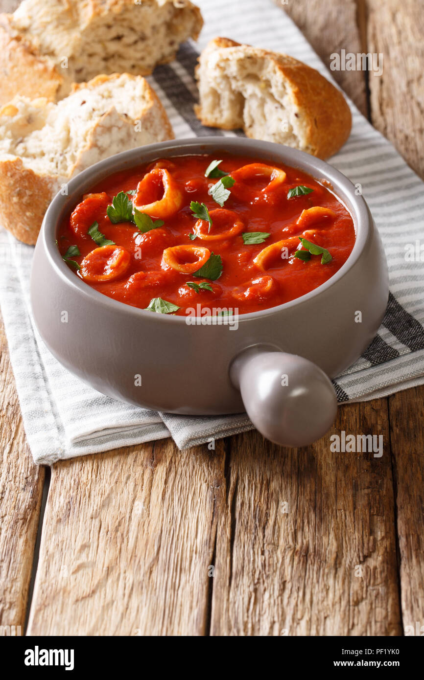 Leckeren Tintenfischringe in Tomaten mit Gewürzen und Petersilie close-up in einen Topf mit Brot. Vertikale Stockfoto