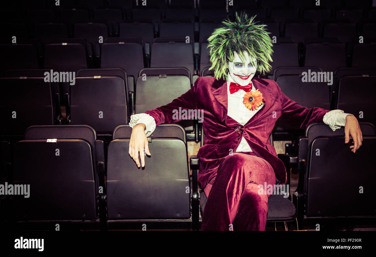 Eine männliche Cosplayer gekleidet, wie der Joker aus Batman und DC Comics Franchise allein in einem verlassenen Kino und Suchen bedrohliche Stockfoto