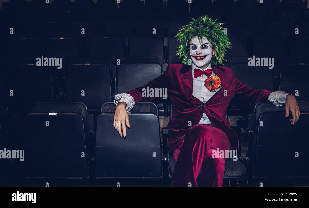 Eine männliche Cosplayer gekleidet, wie der Joker aus Batman und DC Comics Franchise allein in einem verlassenen Kino und Suchen bedrohliche Stockfoto