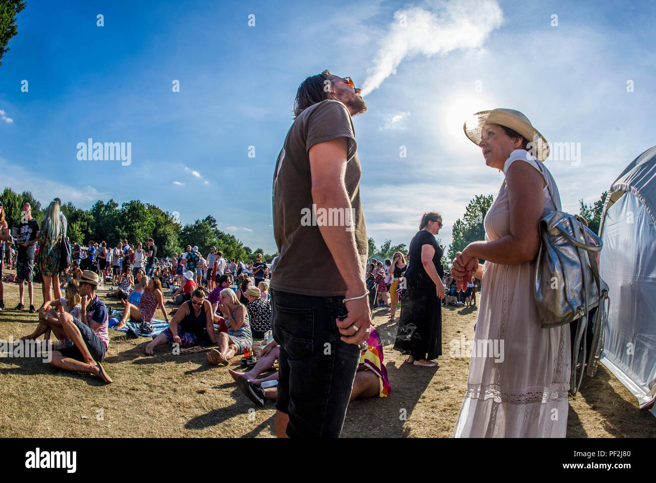 Ein Mann vaping Gespräche zu einer Dame in einem breitrandigen Hut an einem Open Air Festival an einem heißen Tag in London. Stockfoto