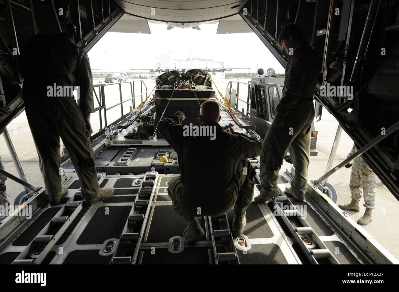 Us Air Force Airman 1st Class Nathaniel Monroe (Mitte), 156 Airlift Squadron Lademeister, gibt der Hand und des Arms Signale die Bewegung einer Palette lader fahrzeug zu lenken, da es Ansätze einer C-130 Hercules Flugzeuge auf der North Carolina Air National Guard Base, Charlotte Douglas International Airport, N.C., Feb 6, 2016. Die Palette ist Teil eines MAX Formationsflug und Air Drop Training Mission an der Stanley County Airport, New London, N.C., die jedes Flugzeug und Paletten an die 145 Luftbrücke Flügel zugeordnet. (U.S. Air National Guard Foto: Staff Sgt. Julianne Showalter) M. Stockfoto