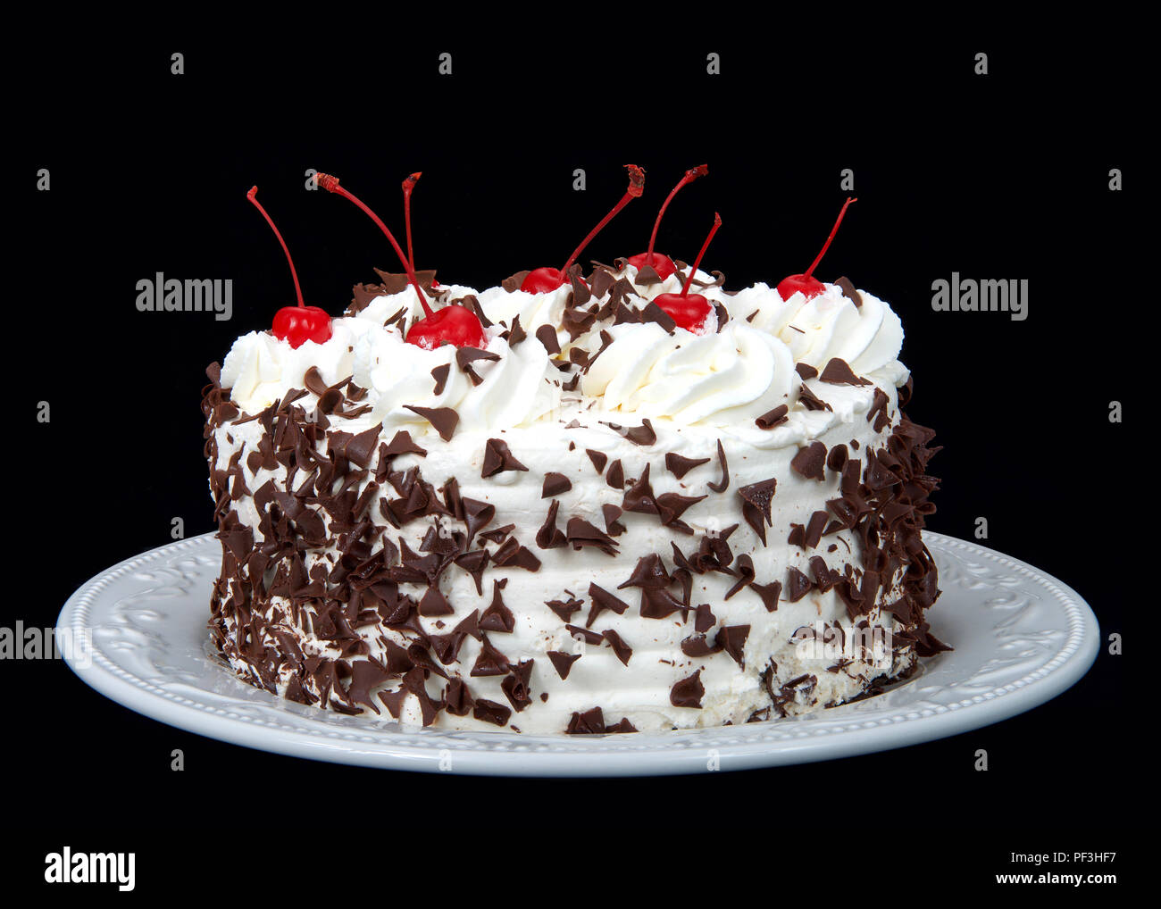 Schwarzwälder Kirschtorte auf einem weißen Teller auf einem dunklen Hintergrund. Schlagsahne, rasiert Praline, die Kirschen auf der Oberseite. Stockfoto