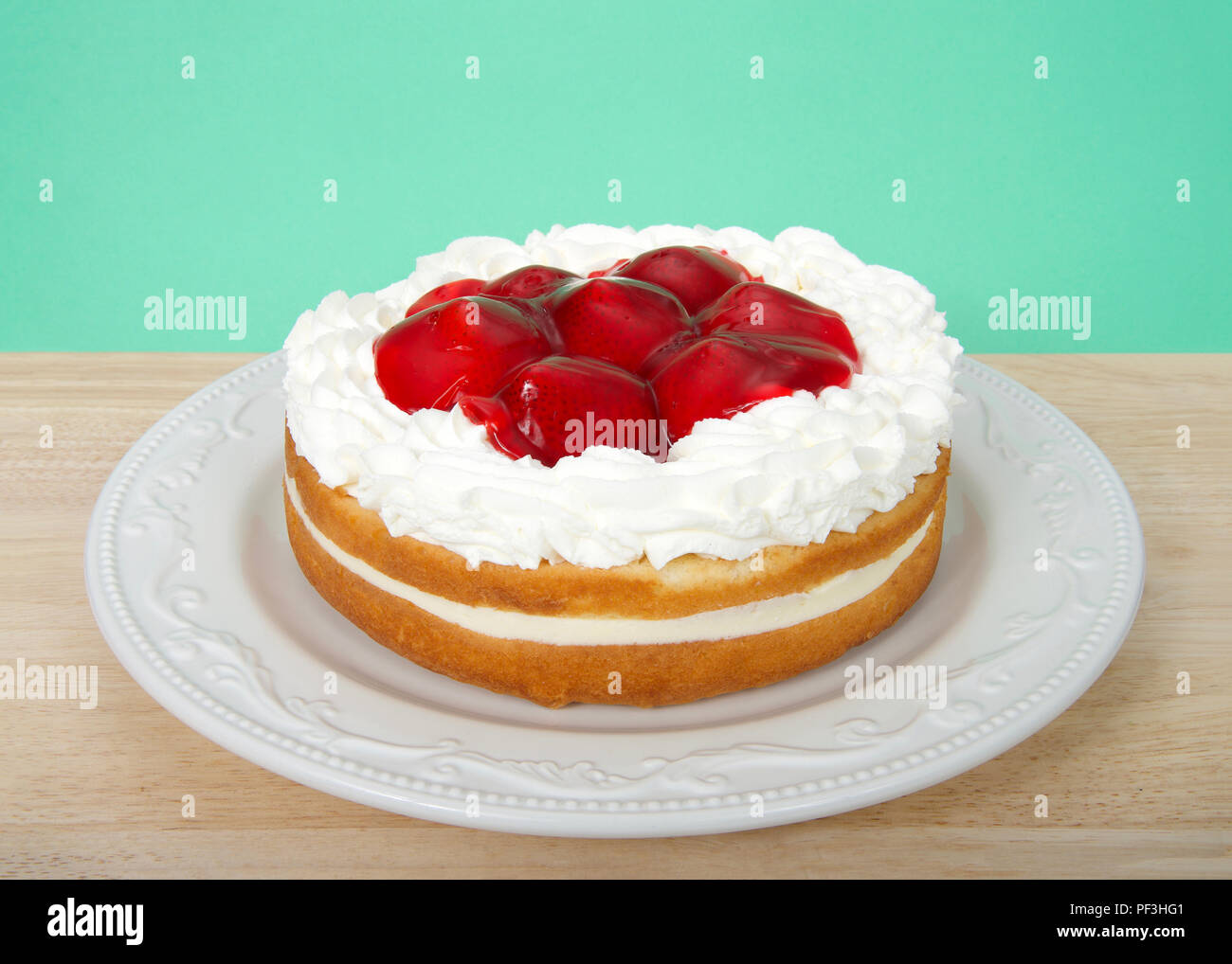 Licht erfrischenden Vanille Kuchen mit Sahne füllen, garniert mit Sahne und verglaste ganze Erdbeeren auf einem hellen Holz Tisch mit Hellgrün hinterg Stockfoto