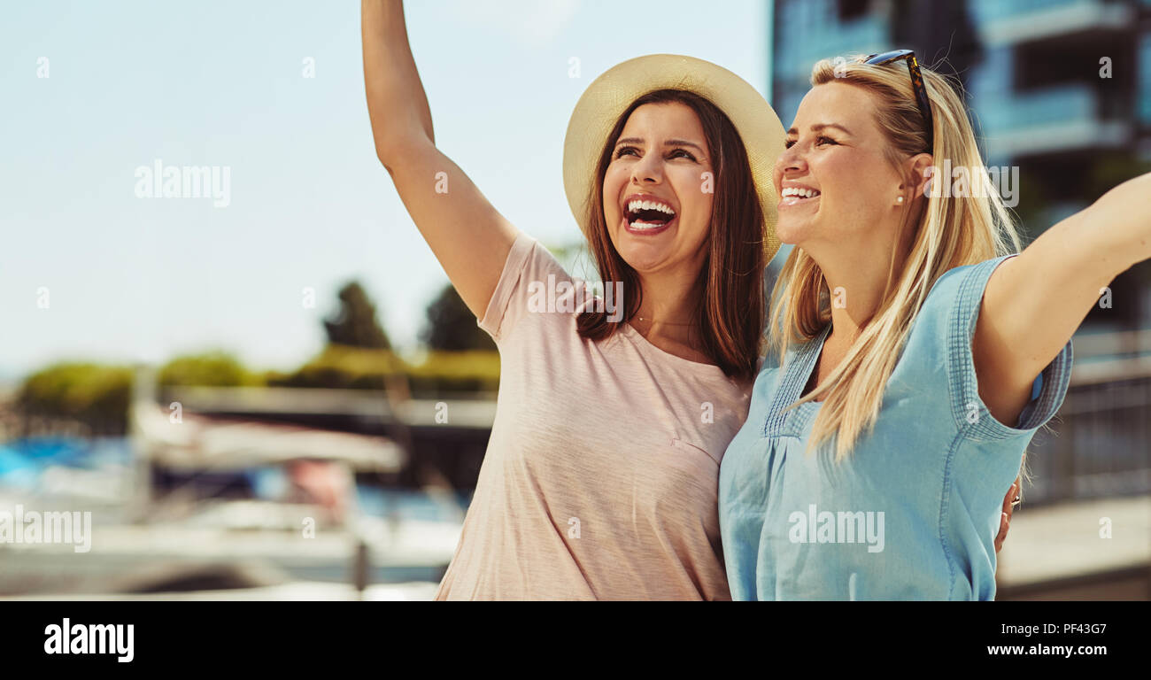 Zwei lachende Junge weibliche Freunde stehen, Arm in Arm, während eine gute Zeit zusammen, die in der Stadt im Sommer Stockfoto
