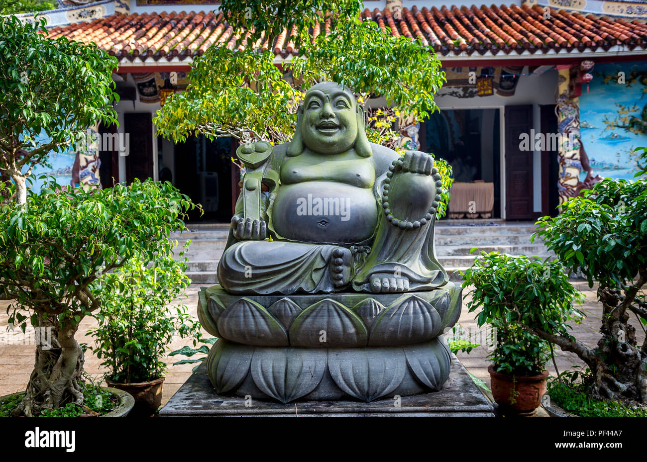 Ein Big Fat Buddha mit kleinen Pflanzen und Bäume vor einem Tempel, eine beliebte Touristenattraktion südlich von Hue, Vietnam. Stockfoto