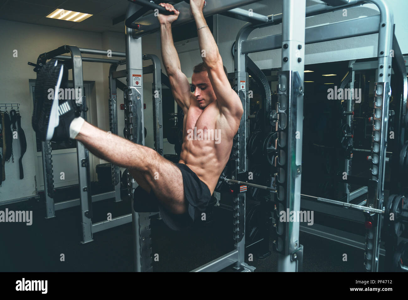 Fitness Mann hängen an horizontalen Balken Beine darstellenden wirft, in der Turnhalle Stockfoto