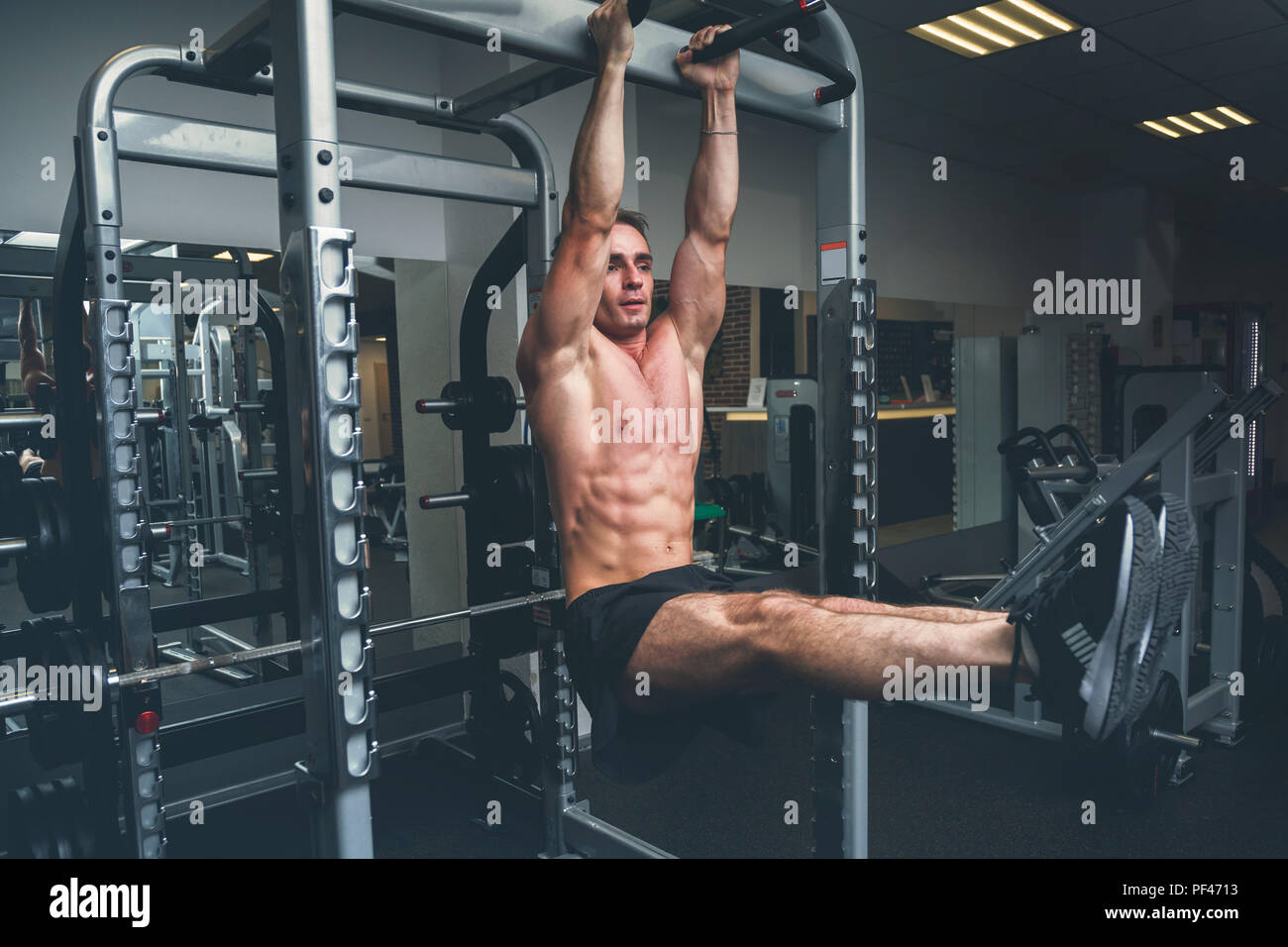 Fitness Mann hängen an horizontalen Balken Beine darstellenden wirft, in der Turnhalle Stockfoto