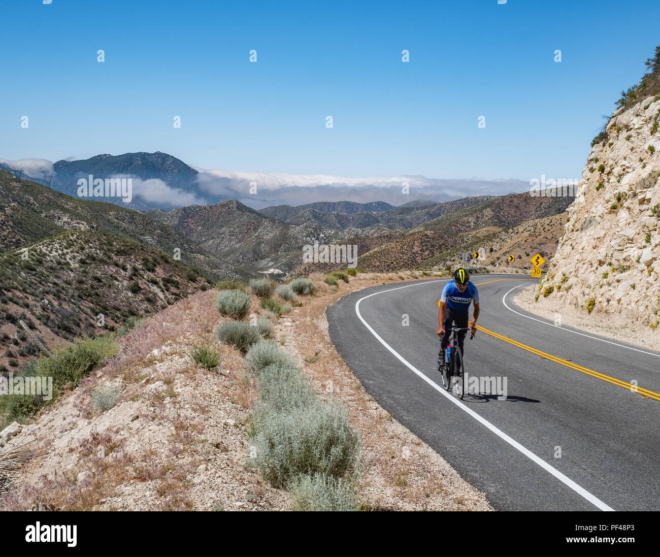 Ein unerschrockener Radfahrer schiebt eine lange Grad auf dem Angeles Wald Autobahn im ANF. Ein Höhepunkt der San Gabriel Mtns ist im Hintergrund sichtbar. Stockfoto